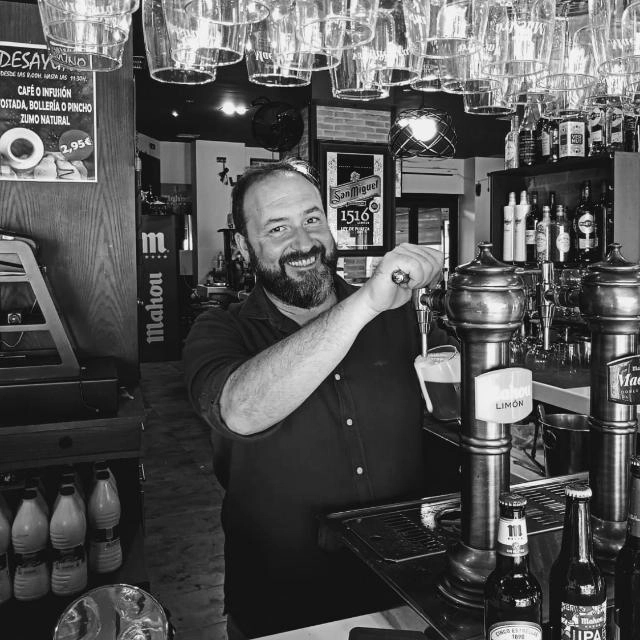 Camarero sirviendo cerveza en un bar con una sonrisa.