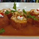 Rollitos rellenos de marisco rebozados, servidos con salsa americana y decorados con mayonesa y un toque de salsa picante.