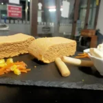 Pastel de cabracho cortado en dos porciones, acompañado de palitos de pan, zanahoria y maíz, con un bol de mayonesa.