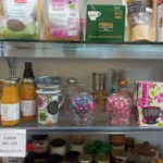 Estantería con productos ecológicos, infusiones, azúcar de caña, zumos bio y tazas decoradas en una tienda natural.