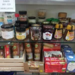 Estantería con productos ecológicos, miel, jengibre bio, cacao, galletas de espelta y tés naturales en una tienda saludable.