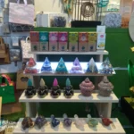 Expositor con pirámides energéticas, conos de incienso, figuras de minerales y cajas de sahumerios en una tienda ecológica.