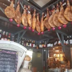 Jamones curados colgados en el interior de un bar tradicional junto a botellas de vino.