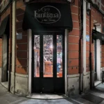 Entrada iluminada del bar-tienda L’Antigua en Langreo durante la noche.